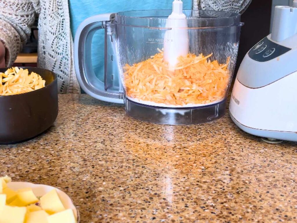 A woman adding grated cheese to a food processor.