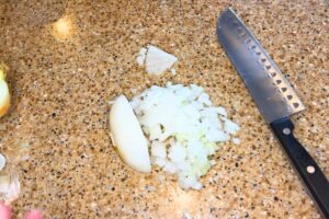 An onion diced on a countertop. There is a knife off to the side.