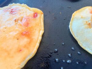 Cooked pancakes with strawberries inside on a black griddle.