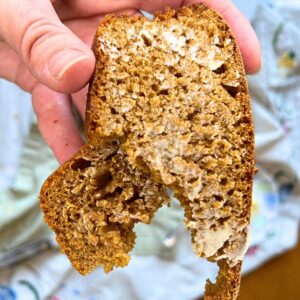 A woman holding a torn slice of brown bread with butter spread on it.
