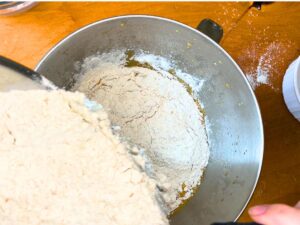 A dry flour mixture being added to a metal bowl with a brown liquid inside.