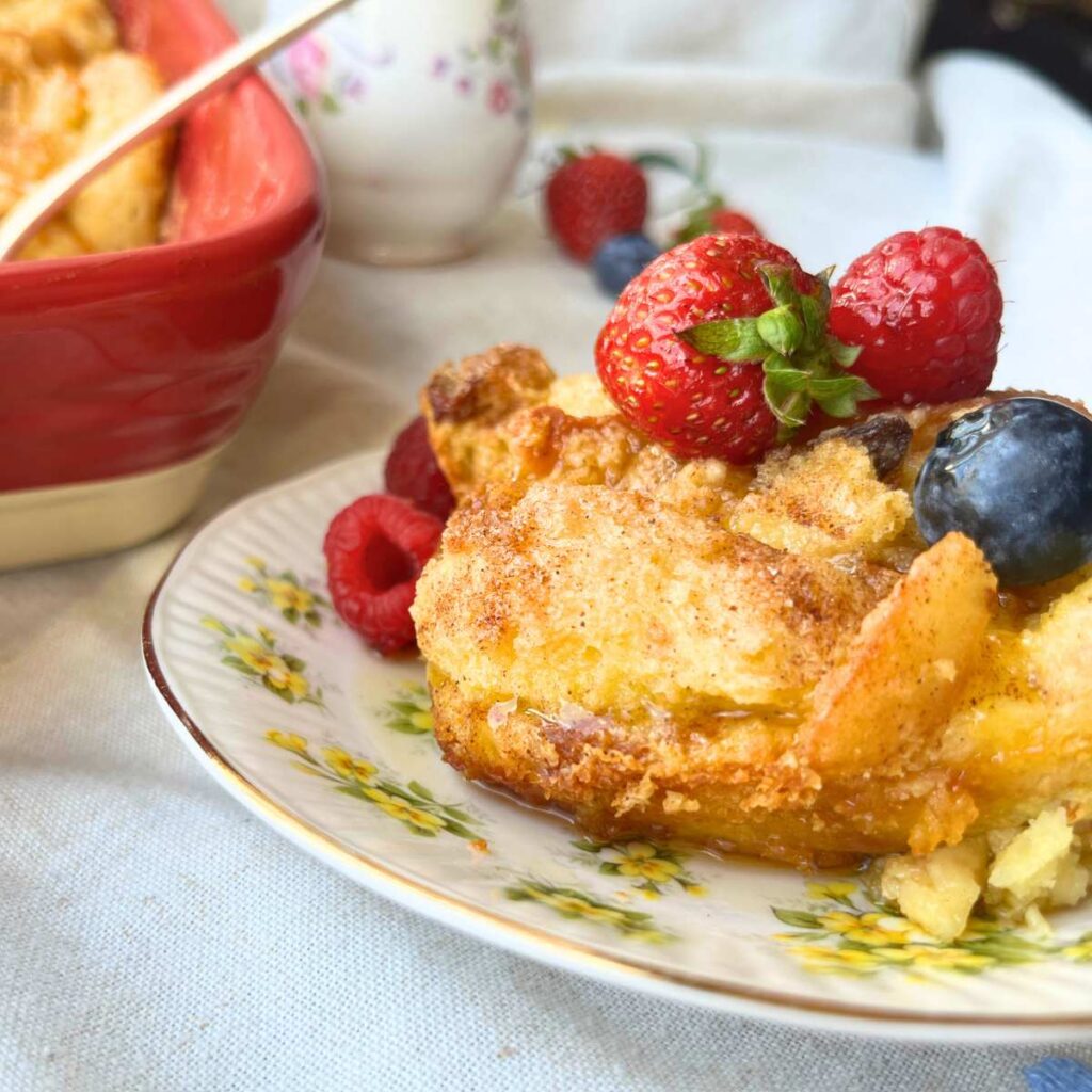 A breakfast casserole on a yellow floral plate with berries on top. The full casserole is in the background.