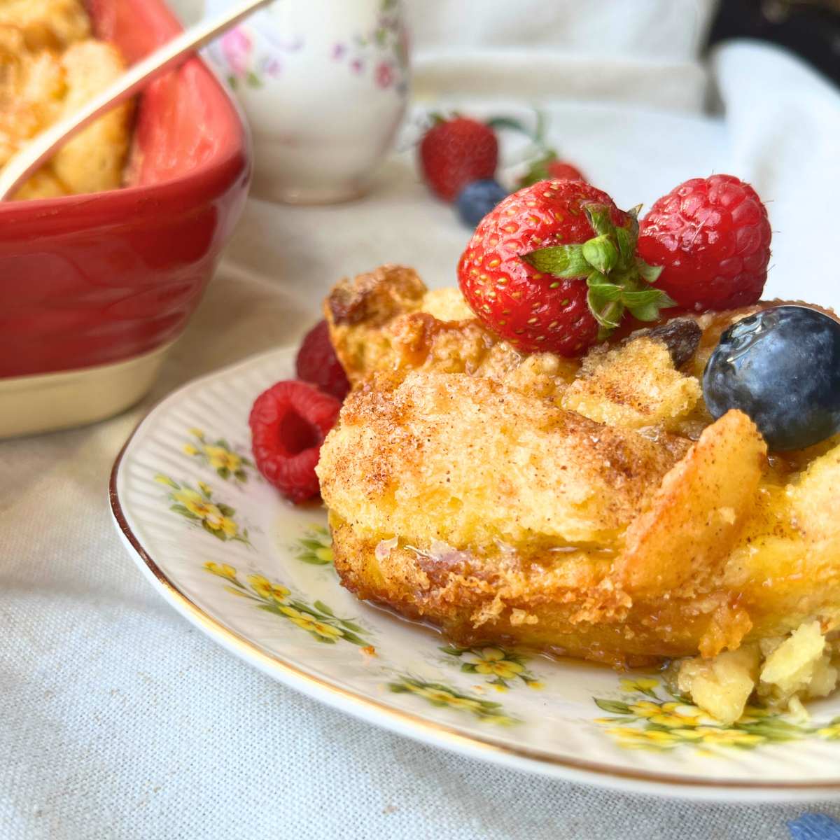 A breakfast casserole on a yellow floral plate with berries on top. The full casserole is in the background.