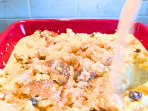 A woman pouring cinnamon sugar on top of a French toast casserole.