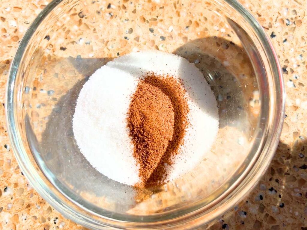 A small glass bowl with sugar and cinnamon inside.