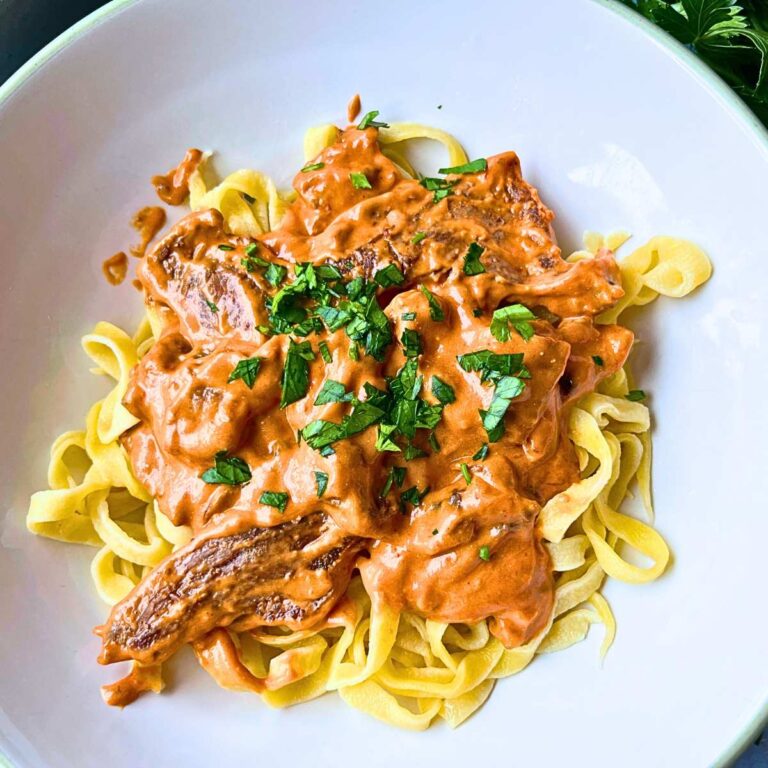 A large white bowl with pasta topped with beef stroganoff.