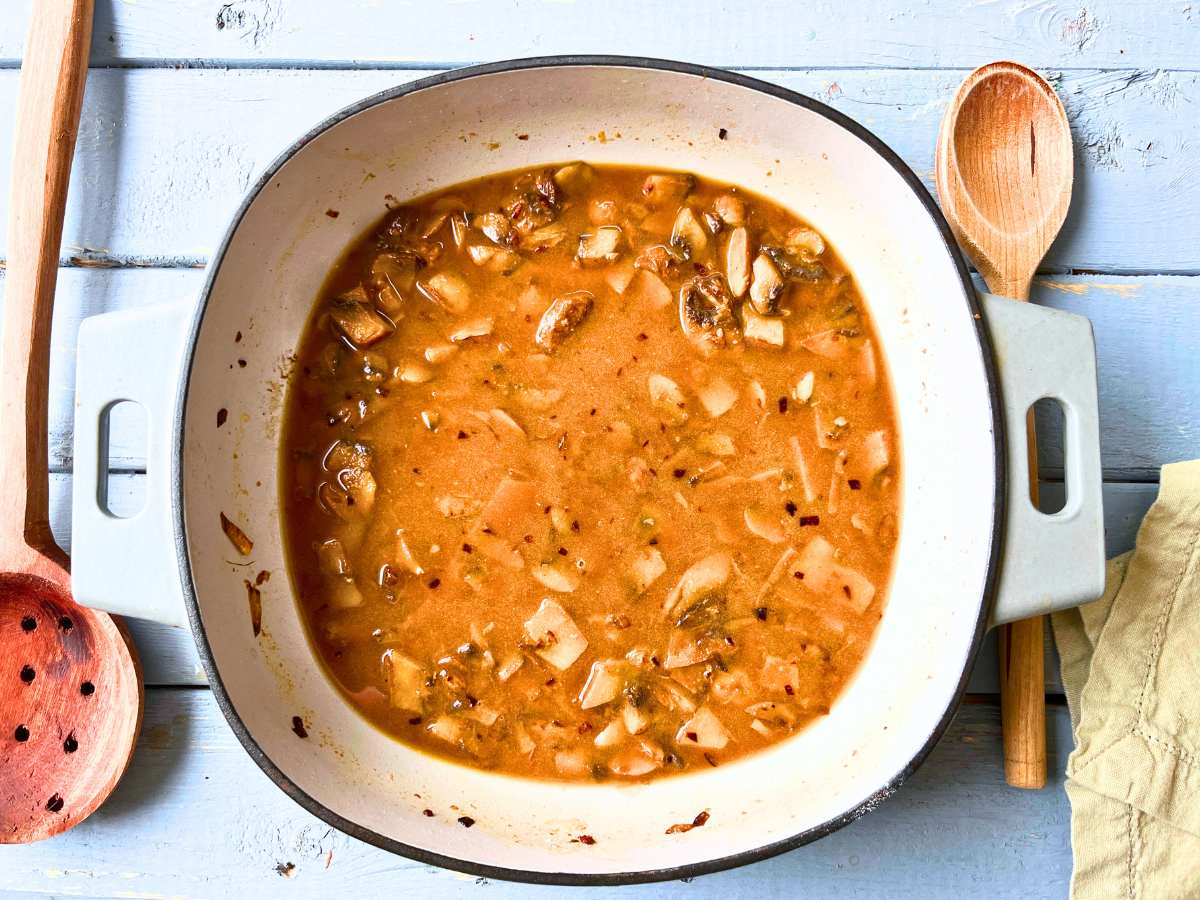 A Dutch oven with cooked mushrooms, onions, and beef stock inside.