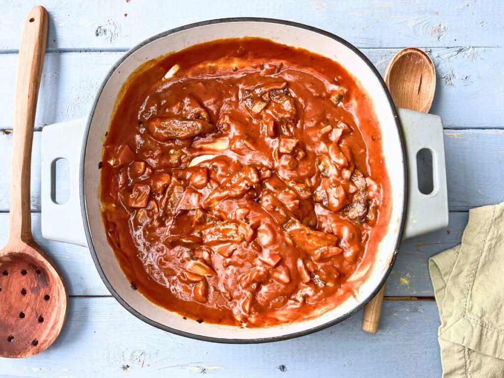 A Dutch oven with a tomato beef sauce inside.