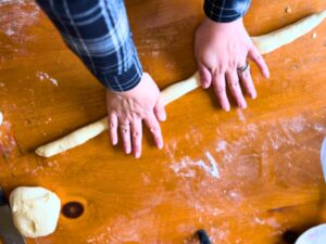 A woman rolling dough into a long rope shape.