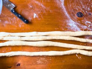 Four ropes of dough on a wooden table.