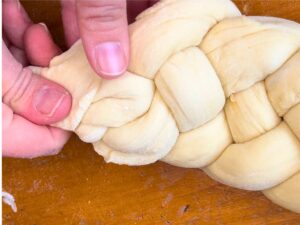 A woman pinching the end of a dough braided bread loaf together.