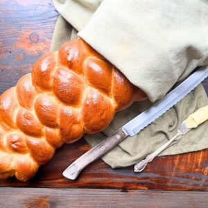 A braided bread loaf wrapped in linen. There is a bread knife and a butter knife on the side.