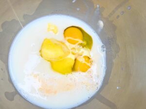 Milk, yeast, eggs, and butter inside of a metal bowl.