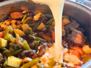 Woman adding crean to a pot of beef stew