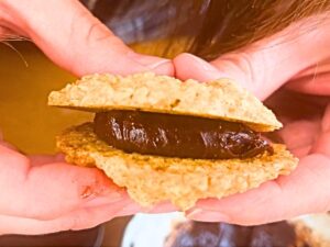 There is a woman squeezing chocolate inside of two oatmeal cookies.