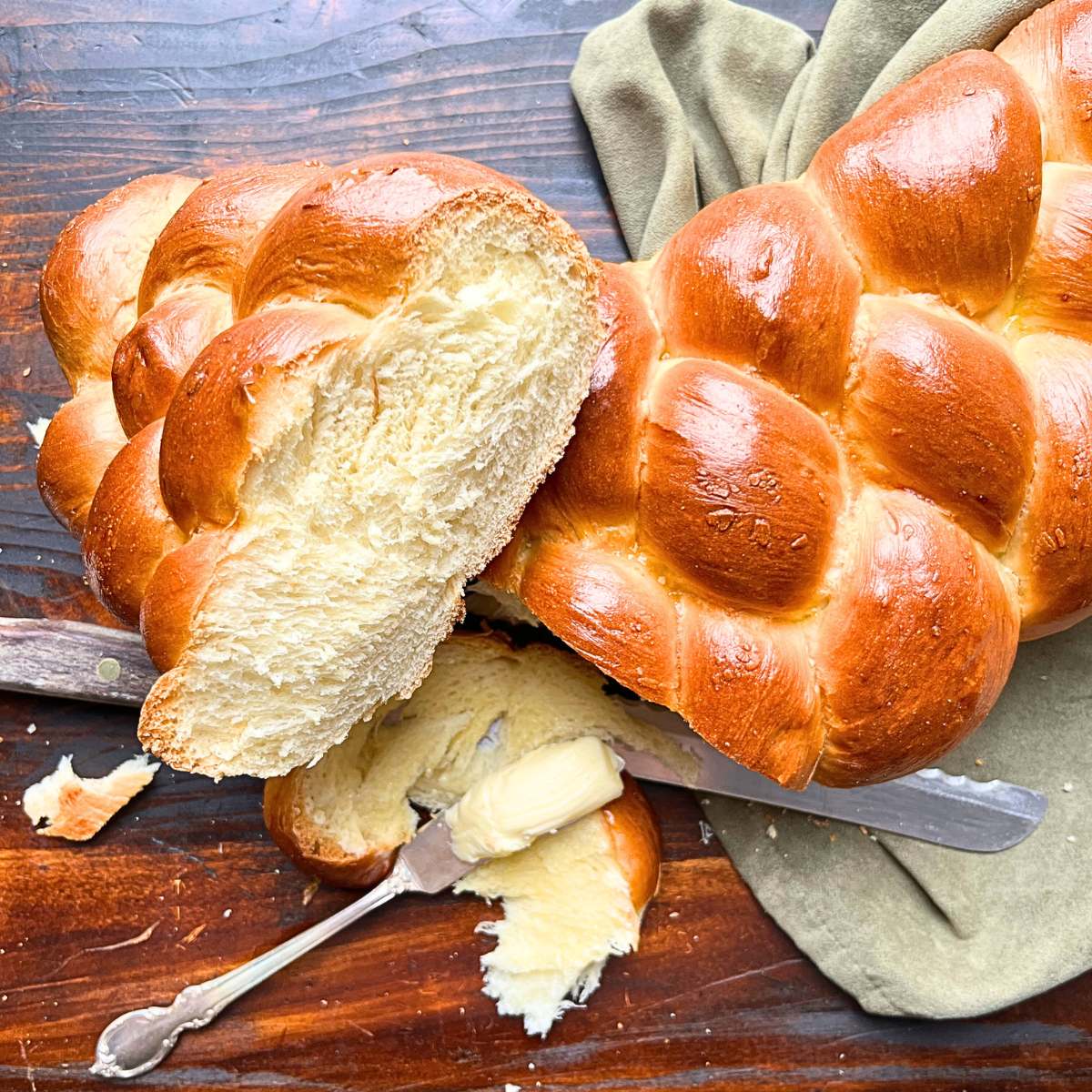 A braided bread loaf that has been but to show the inside. There is a knife with butter on it.