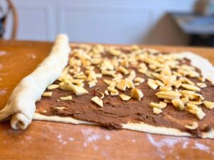 A partially rolled rectangle of dough with a brown spread and chopped apples inside.