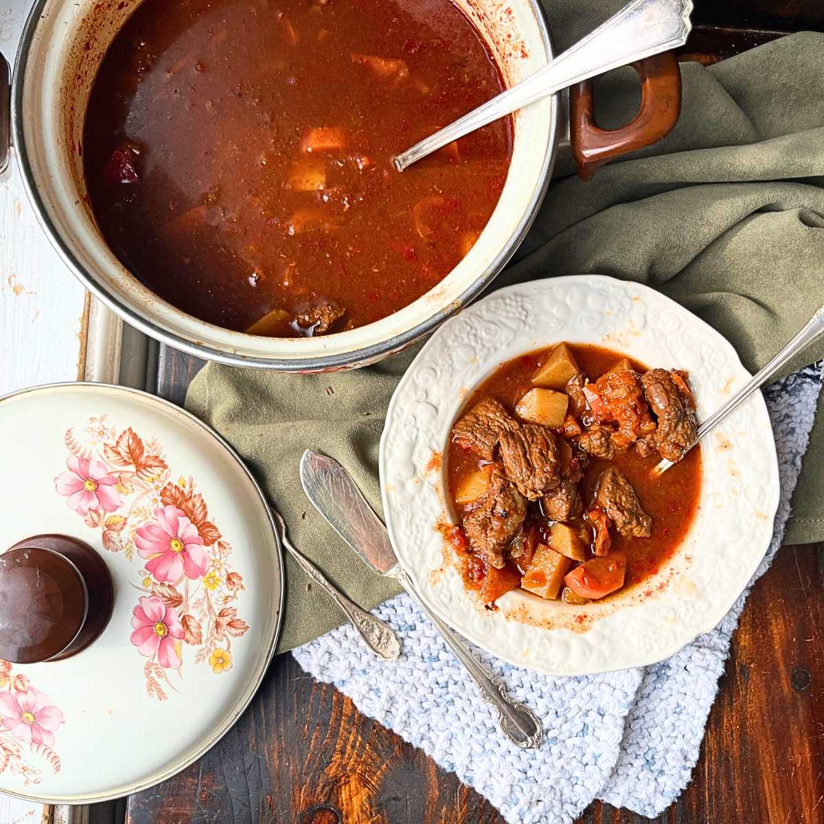 A pot of tomato beef and vegetable soup. There is a bowl of soup in front 