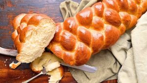 A long braided loaf of bread. Part of it is sliced. There is a knife with butter on it.