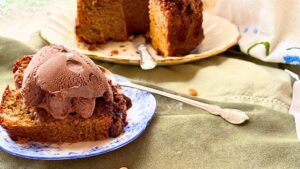 There is a cake on a floral platter. There are slices removed. There is a slice in front with chocolate ice cream on top.