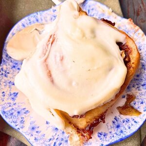 A close up look at a cinnamon roll with white icing on top. It is on a blue floral plate