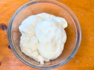 A glass bowl with bread dough inside.