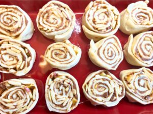 unbaked cinnamon rolls in a red rectangular casserole dish.