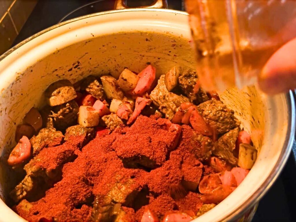 A woman adding paprika to a pot of beef and vegetables