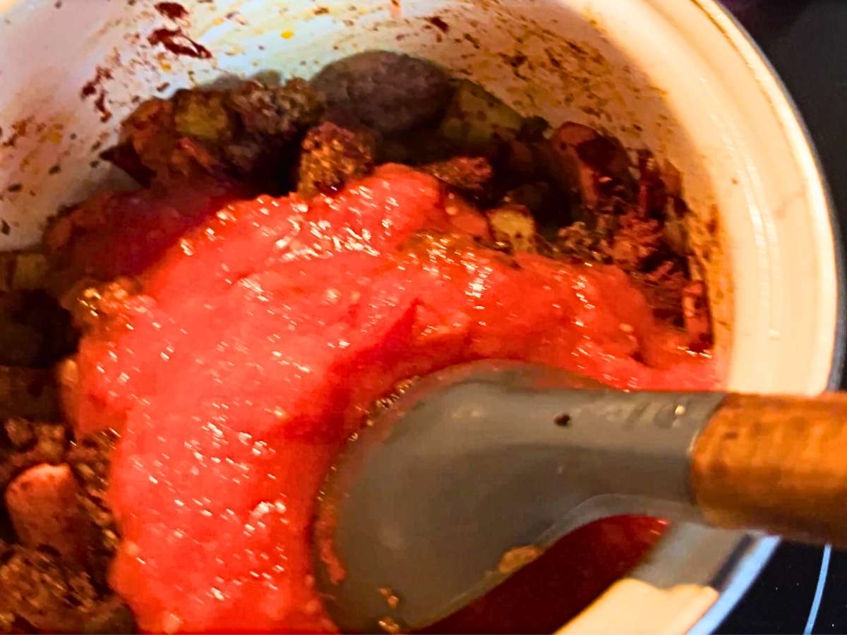 A woman adding tomato sauce to a pot of beef and vegetables