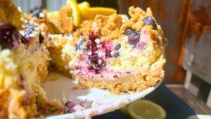 There is a blueberry cheesecake on a cake stand. There is a slice out of it.