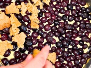 A woman placing cookie pieces on top of a cooked blueberry cheesecake.