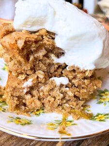 There is a slice of rhubarb cake on a yellow floral plate. There is a scoop of vanilla ice cream on top.