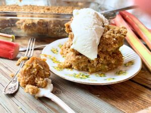 Rhubarb cake on a yellow floral plate with vanilla ice cream on top. In the background is more of the cake. There is a spoonful of cake beside.