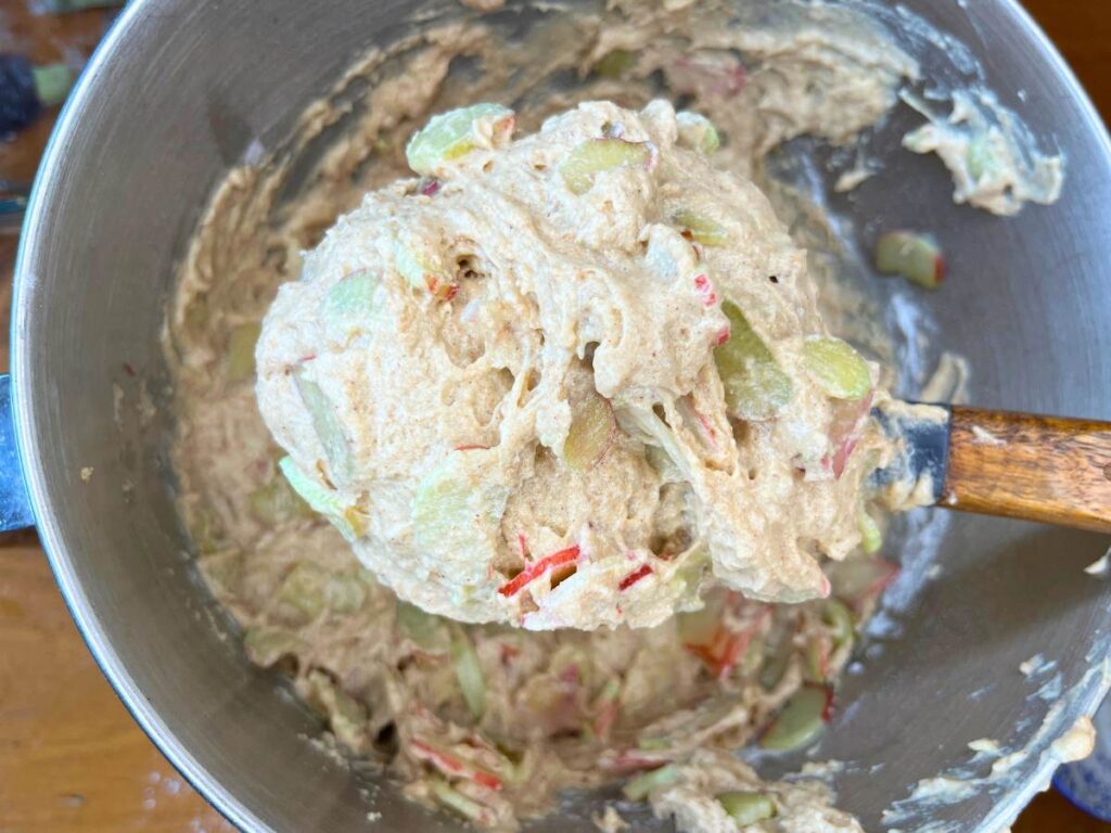 A woman mixing rhubarb into batter in a metal bowl.