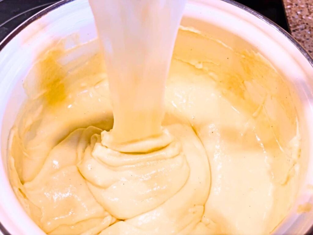 A woman pouring a creamy white sauce into a white sauce pot.