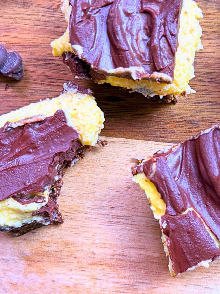Three Nanaimo bars on a wooden surface one has a bite out of it.