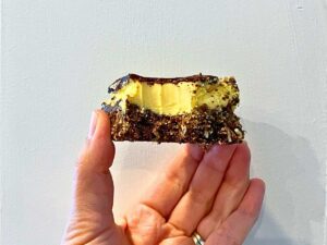 A woman is holding a Nanaimo bar with a bite out of it.