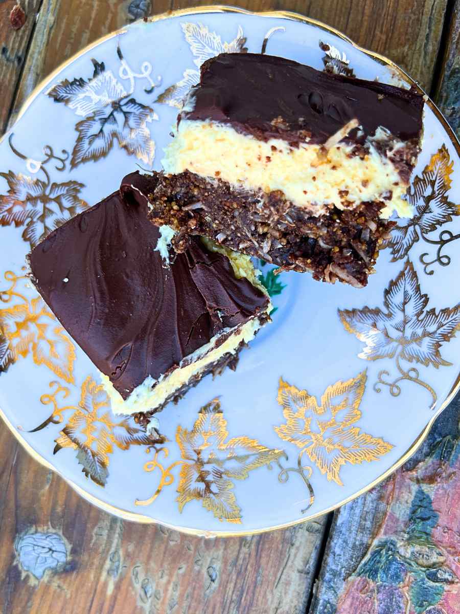 A close up look of two Nanaimo bars on a gold maple leaf plate.