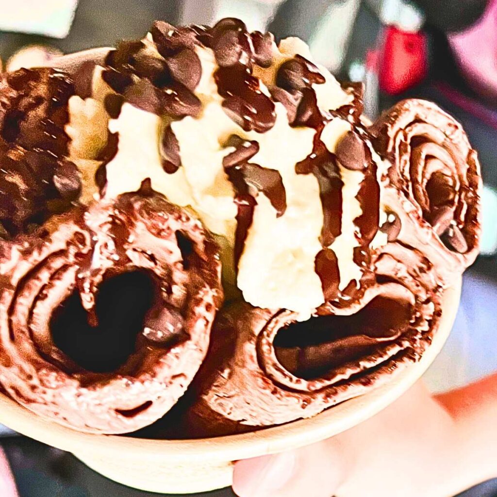 A bowl of rolled ice cream. There is whipped cream and chocolate chips on top.