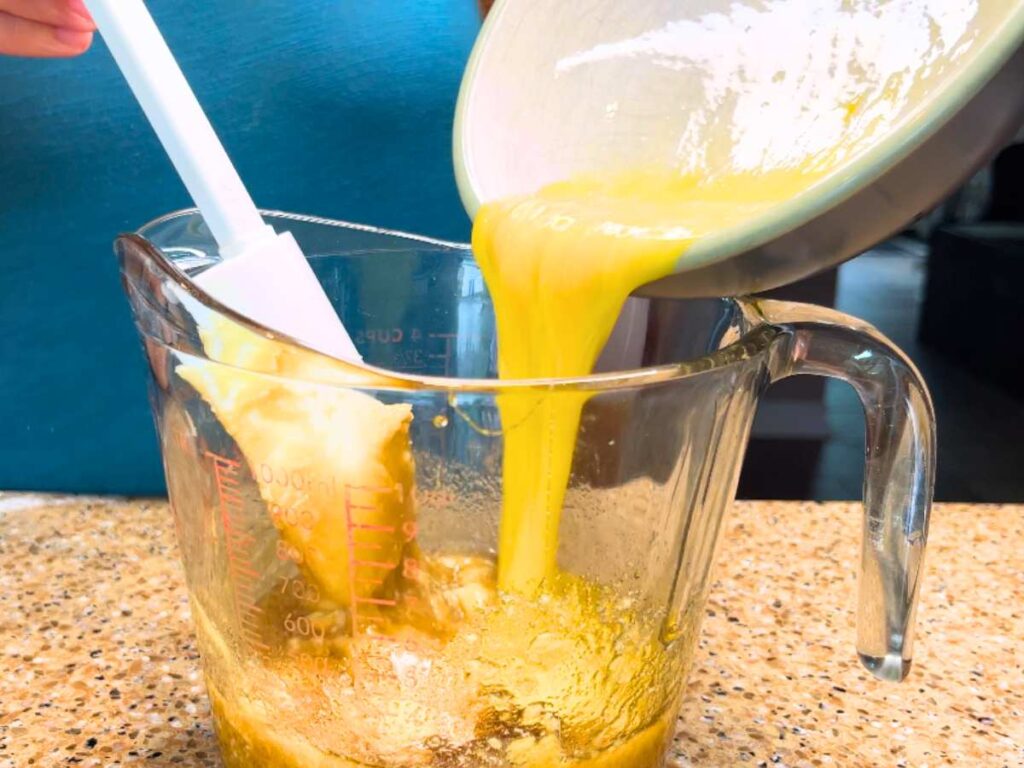 A woman pouring beaten eggs into a large glass measuring cup.