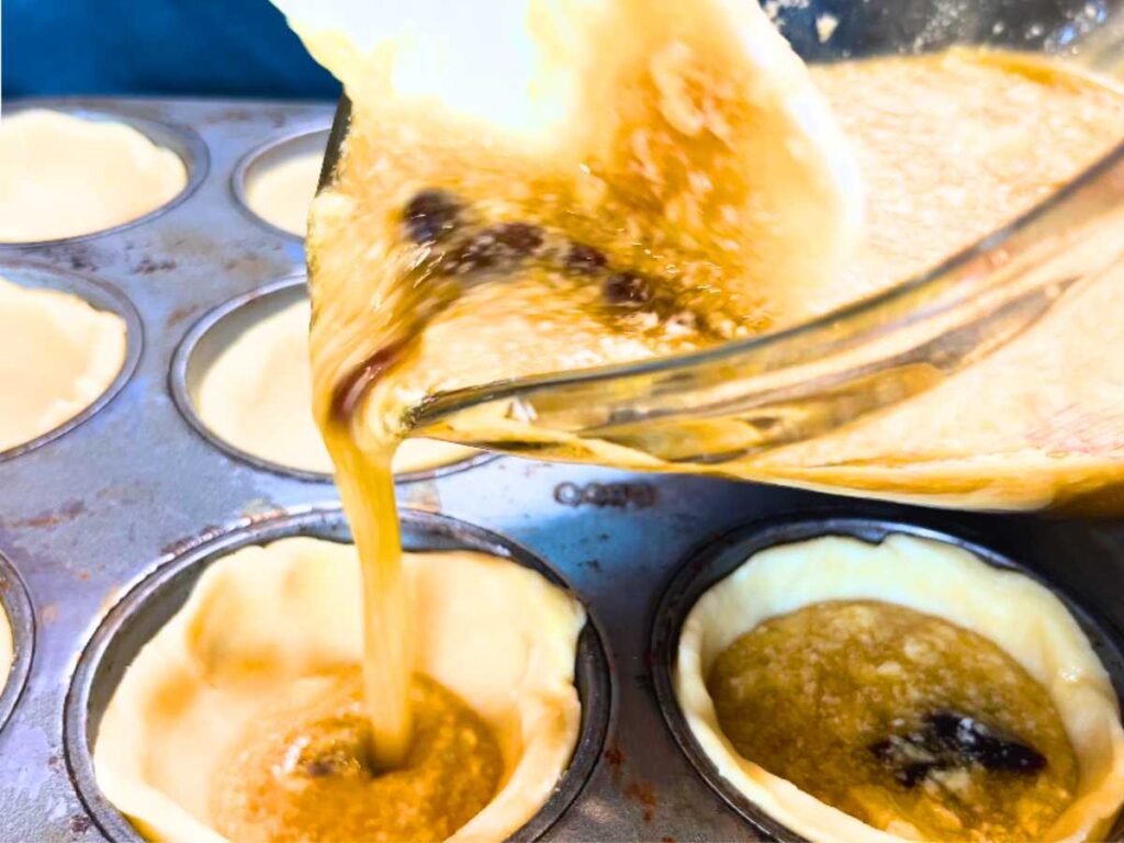 Woman pouring filling into tart shells.