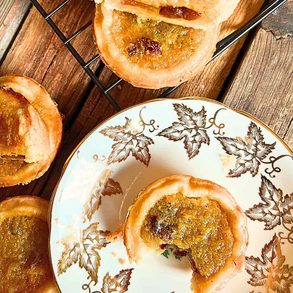 Buttertarts on a wooden table. There is one on a golden maple leaf plate. There is a bite out of it.