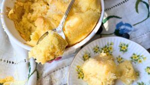 A cheese soufflé with a spoon resting on top. There is some of the soufflé on a yellow floral plate.