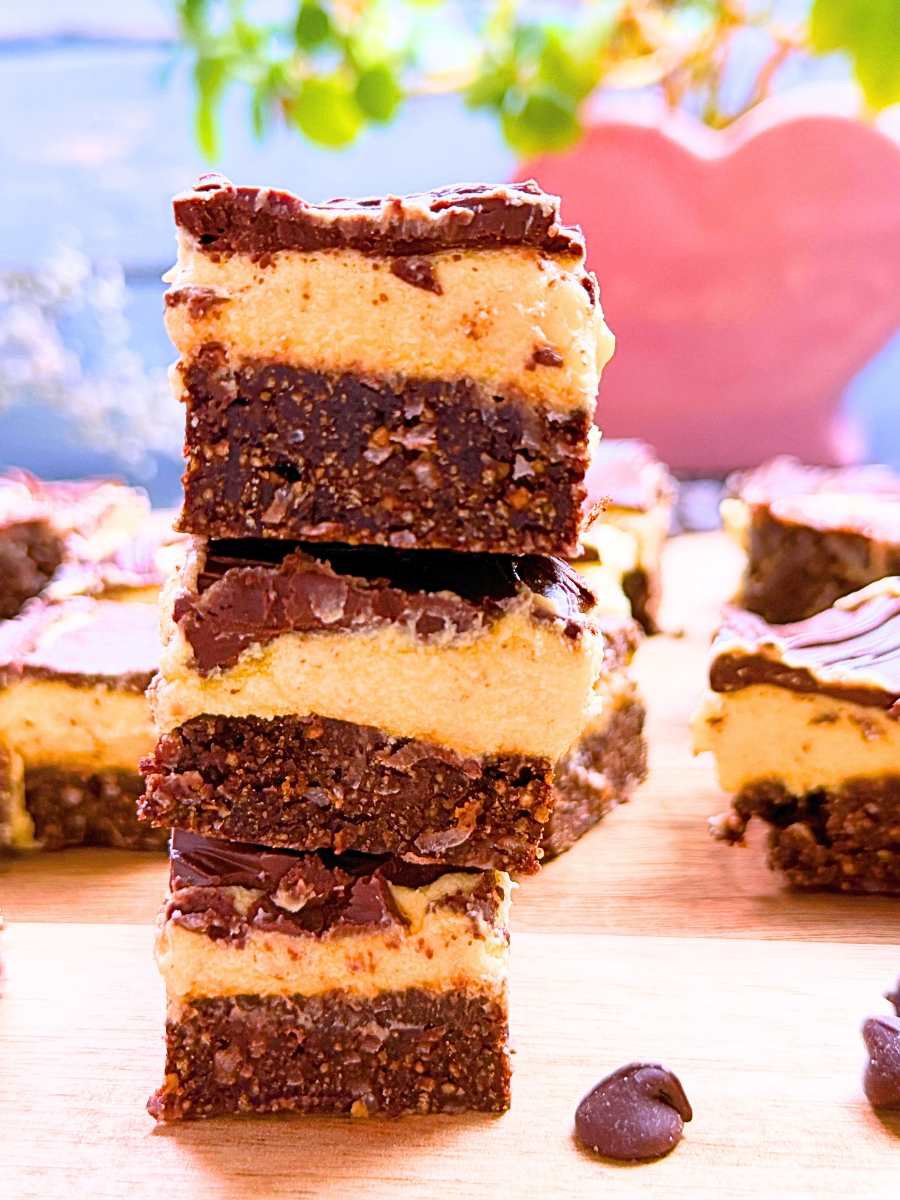 Three Nanaimo bars stacked to show their coconut-graham-cracker-chocolate layer, the custard layer, and the chocolate top.