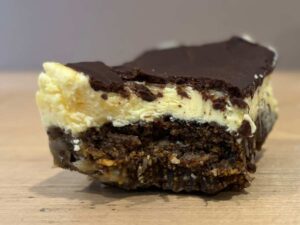 A Nanaimo bar on a wooden counter. There is a bite out of it.
