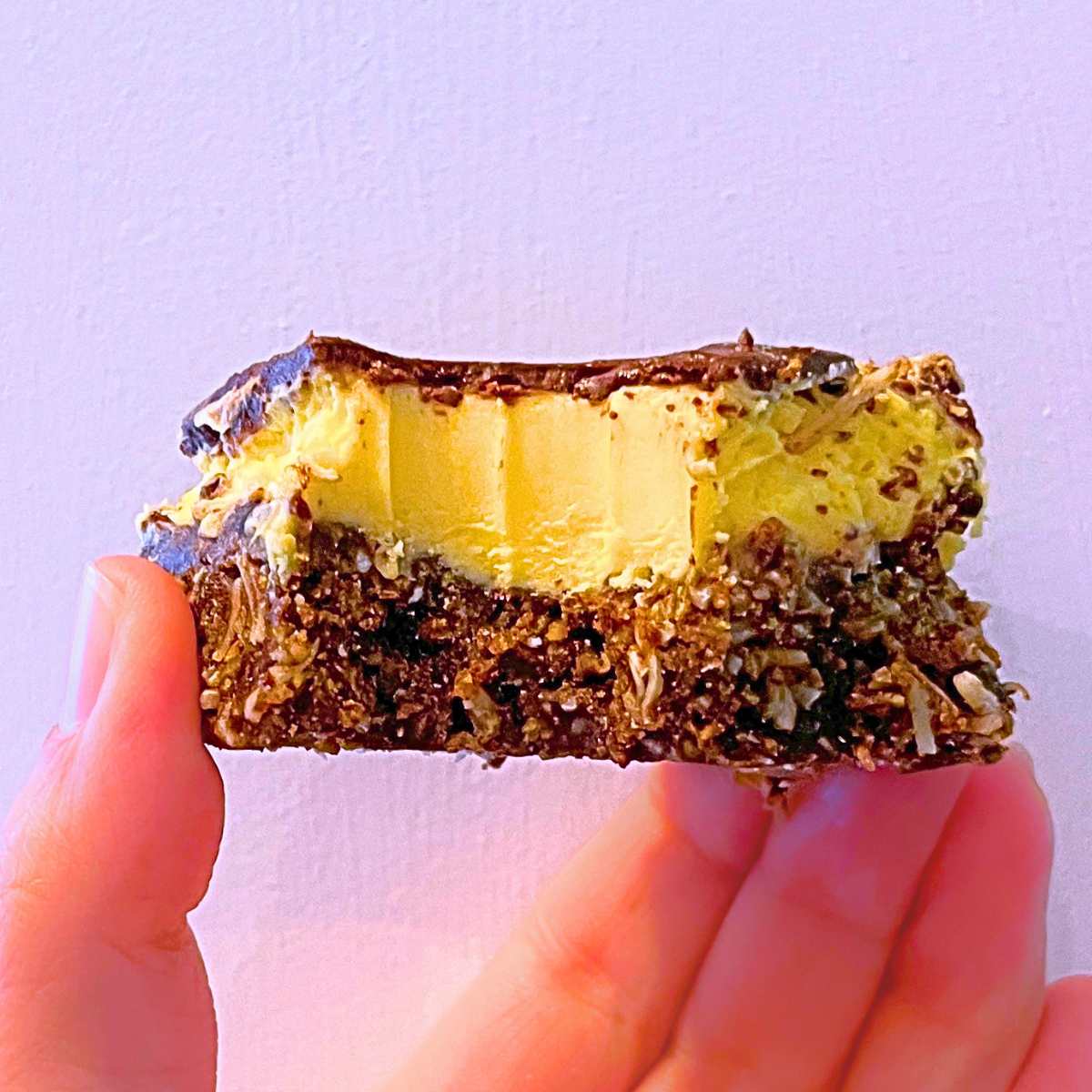 A woman is holding up a Nanaimo bar with a bite out of it.