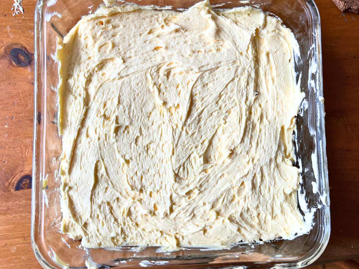 A pale yellow custard icing spread into the bottom of a glass casserole dish.