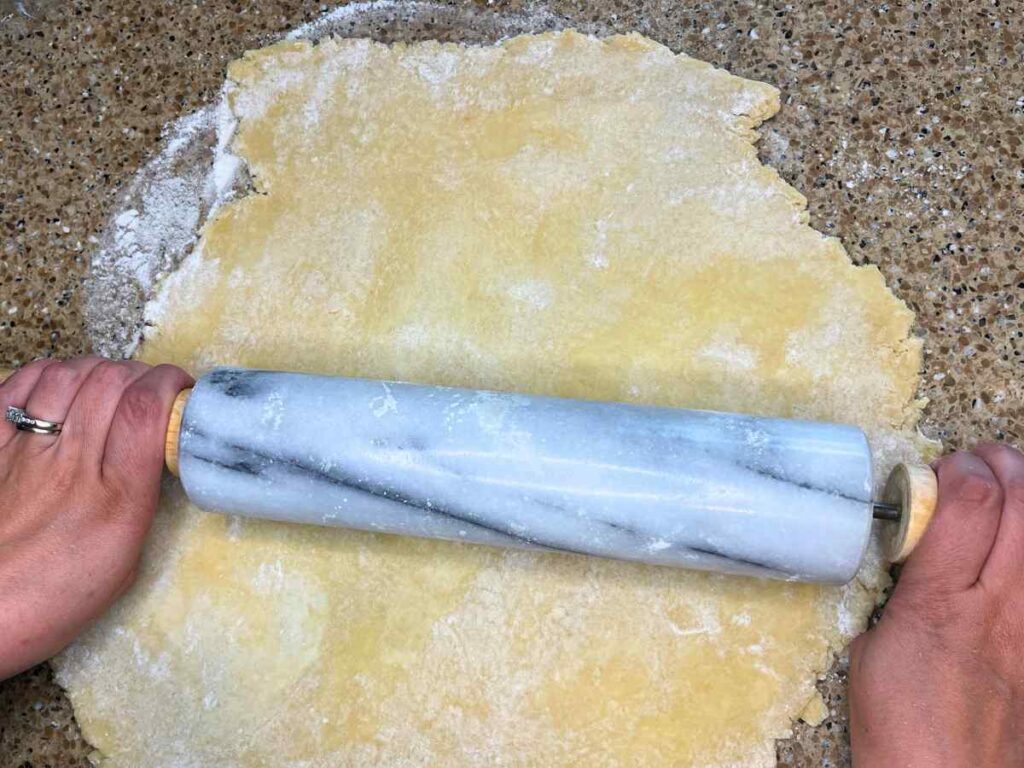 A woman is rolling out pie dough with a marble rolling pin.