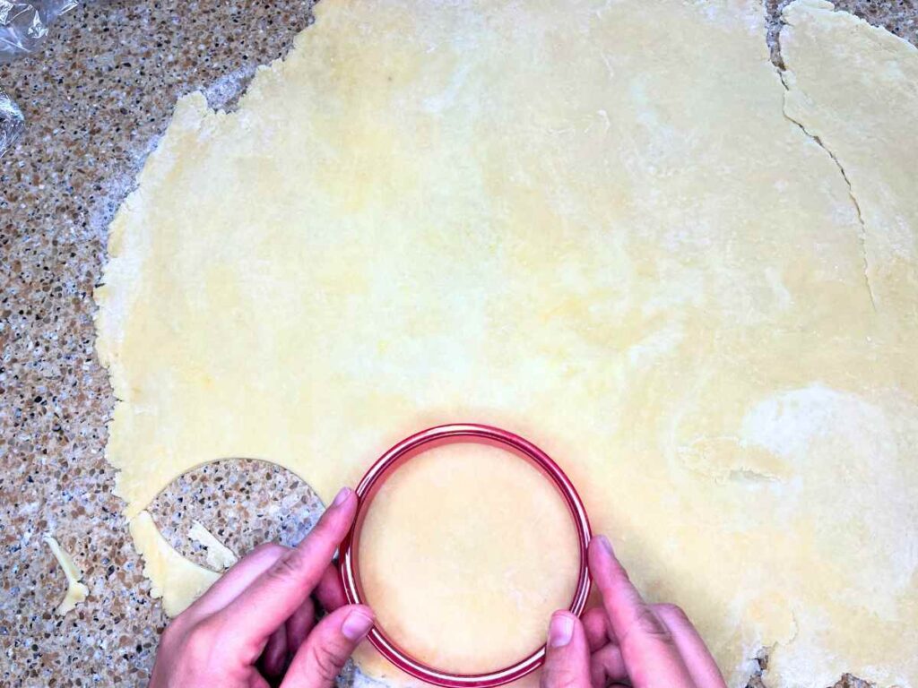 A woman is cutting dough using a circle cookie cutter.