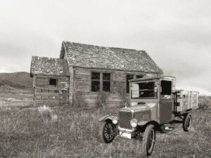 An old wooden house with an old car parked in front. Black and white photo.